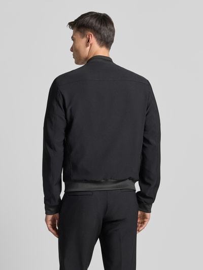 Männermodel trägt schwarzen Blouson mit seitlichen Eingrifftaschen von MCNEAL, Material-Mix, Stehkragen, elastische Abschlüsse, Ganzkörperansicht Rückansicht