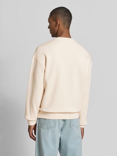 Männermodel trägt Relaxed Fit Sweatshirt aus reiner Baumwolle Modell 'WORDMARK' von ARMEDANGELS in Creme zu hellblauen Jeans, Ganzkörperansicht Rückansicht.