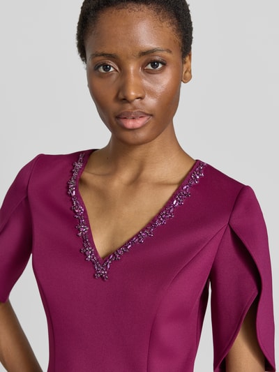 Frauenmodel trägt Knielanges Kleid mit Ziersteinbesatz von Adrianna Papell in dunklem Pink, V-Ausschnitt, 1/2-Arm, taillierte Passform, Nahaufnahme Oberkörper. Rückenlänge 102 cm, Brustweite 37 cm, Ärmellänge 32 cm.