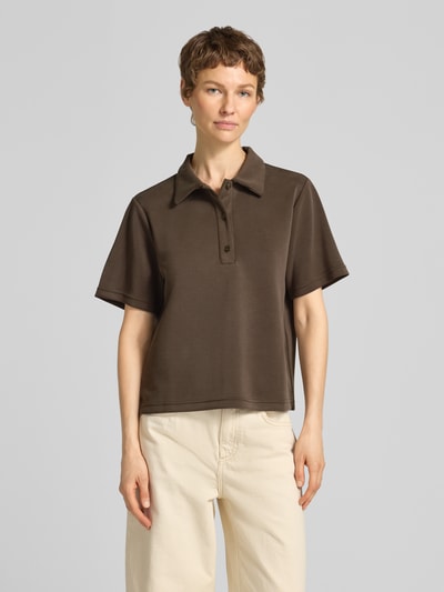 Kobiece model nosi koszulkę polo Loose Fit Poloshirt mit kurzer Knopfleiste Modell 'Helle' od My Essential Wardrobe, mieszanka materiałów z dodatkiem wiskozy, kołnierzyk polo, krótka listwa guzikowa, długość tyłu w rozmiarze S: 57 cm, brązowy kolor, prosty fason, gładka tekstura. Ganzkörperansicht von vorne.