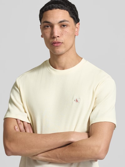 Männermodel trägt Regular Fit T-Shirt mit Logo-Patch von Calvin Klein Jeans in Creme, Baumwoll-Mix, Strukturmuster, Nahaufnahme Oberkörper.