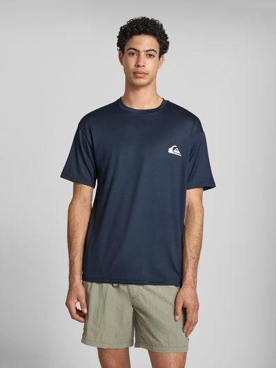 Männermodel trägt T-Shirt mit Rundhalsausschnitt und Logo von Quiksilver, dunkelblau, Regular-Fit, Material-Mix mit Stretch-Anteil, Ganzkörperansicht von vorne. Rückenlänge bei Größe M: 75 cm.