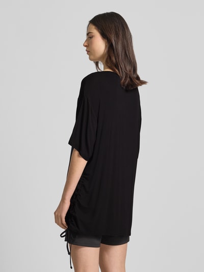 Männermodel trägt T-Shirt mit Logo-Print Modell 'COULISSE' von Guess, czarny, luźny krój, elastyczna mieszanka wiskozy, widoczne marszczenie z tunelem, widok całej sylwetki z tyłu