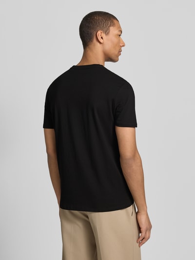 Męski model nosi T-Shirt mit Label-Detail od Guess, czarna bawełna, prosty krój, długość tyłu w rozmiarze M: 69 cm, całopostaciowy widok z tyłu