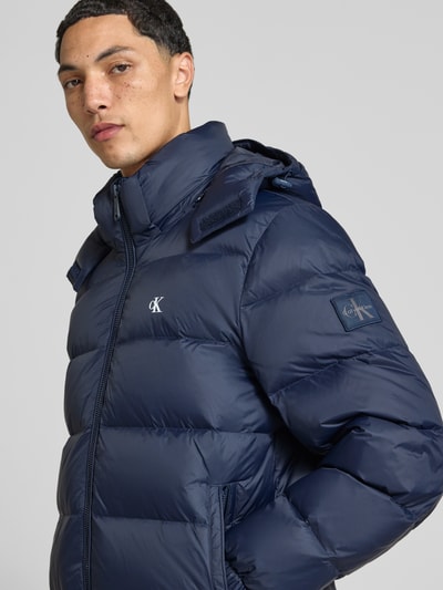 Männermodel trägt Regular Fit Steppjacke mit abnehmbarer Kapuze von Calvin Klein Jeans in Dunkelblau, Nahaufnahme Oberkörper.