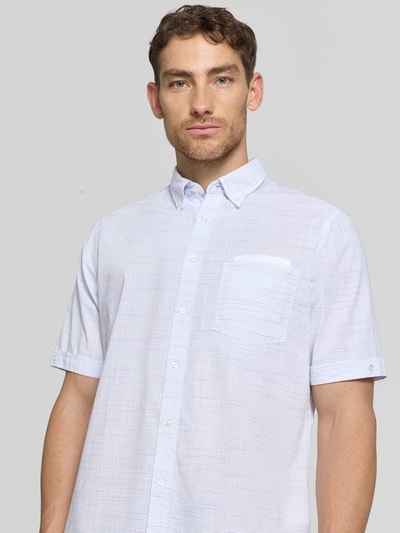 Męski model nosi Regular Fit Freizeithemd mit Button-Down-Kragen od Christian Berg Men, biała bawełna, kieszeń na piersi, krój regular fit, długość tyłu w rozmiarze M: 78 cm, szerokość w rozmiarze M: 44 cm, długość rękawa w rozmiarze M: 26 cm, tekstura delikatnie prążkowana, prosty krój, widoczny przód, zbliżenie na górną część ciała.
