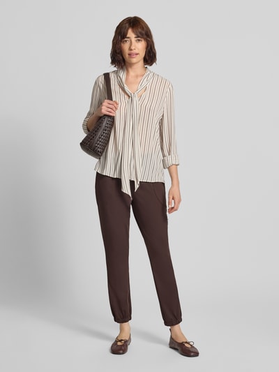 Frauenmodel trägt Jogger Pants mit Reißverschlusstasche Modell 'Jill' von monari in Dunkelbraun, Material-Mix mit Stretch, Ganzkörperansicht von vorne.