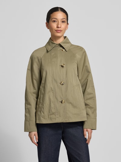 Kobiece model prezentuje kurtkę 'Jacke mit seitlichen Eingrifftaschen und Kentkragen' od Fuchs Schmitt, prosty krój, kołnierzyk typu kent, listwa guzikowa, raglanowe rękawy, wpuszczane kieszenie, długość tyłu w rozmiarze 36: 64 cm, szerokość ramion w rozmiarze 36: 38 cm, szerokość klatki piersiowej w rozmiarze 36: 51 cm, długość rękawów w rozmiarze 36: 44 cm, oliwkowy odcień, gładka tekstura, całkowity widok z przodu.
