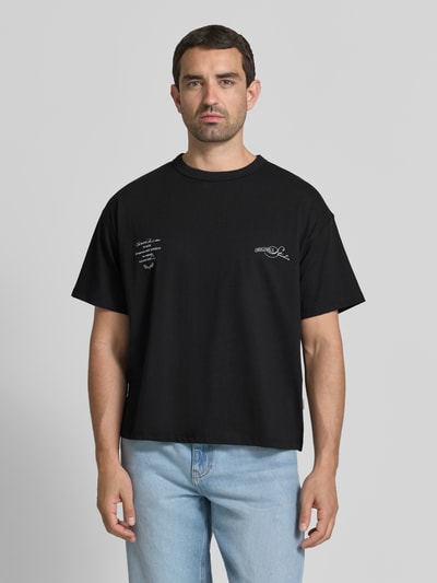 Mężczyznamodel nosi Regular Fit T-Shirt mit überschnittenen Schultern von JACK & JONES, mieszanka bawełny, okrągły dekolt, napis na plecach, tył 66 cm w rozmiarze M, kolor czarny, prostokątne kształty, gładka faktura, Ganzkörperansicht von vorne.