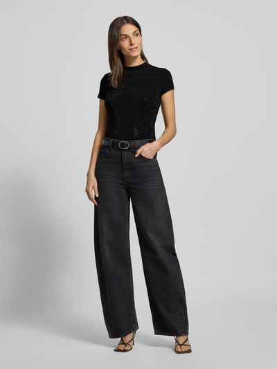 Kobiece model prezentuje Slim Fit T-Shirt mit Allover-Strasssteinbesatz od Guess, czarny kolor, mieszanka bawełny i elastanu, obszycie z kamieni stras, stójka, detal z logo, długość tyłu 51 cm dla rozmiaru S, całkowity widok z przodu.