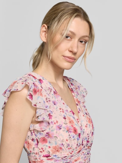Frauenmodel trägt Abendkleid aus Chiffon mit floralem Allover-Print von Jake*s Cocktail, V-Ausschnitt, Kappärmel mit Rüschen-Optik, Taillierte Passform, zartrosa Grundfarbe mit mehrfarbigen Blumen, Stoff mit weicher leicht transparenter Textur, Nahaufnahme Oberkörper.