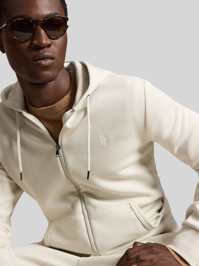 Męski model nosi Regular Fit Sweatjacke aus Baumwoll-Mix od Polo Ralph Lauren, kremowy kolor, gładka tekstura, zbliżenie na górną część ciała.