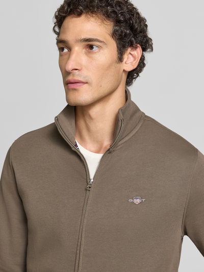 Männermodel trägt Regular Fit Sweatjacke aus Baumwoll-Mix von GANT in Taupe mit Reißverschluss und Logo, Nahaufnahme Oberkörper.