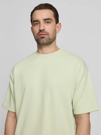 Mannelijk model draagt Oversized T-shirt met ronde hals van Lindbergh in lichtgroen katoenmix met labeldetail, ruglengte maat M: 70 cm. Nahaufnahme Oberkörper.