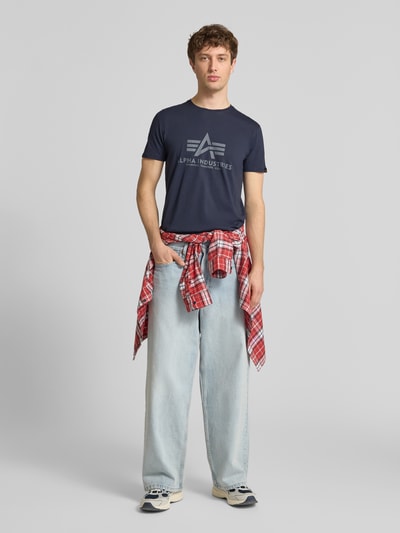 Männermodel trägt Herren T-Shirt mit Label-Detail Modell 'BASIC' von Alpha Industries in Dunkelblau aus Reine Baumwolle, Gerader-Schnitt, Rundhalsausschnitt, Rückenlänge bei Größe M 69 cm, Ganzkörperansicht von vorne.