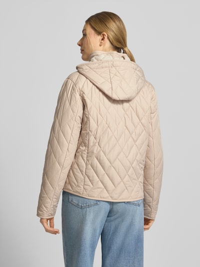 Modelka nosi Steppjacke mit Zweiwege-Reißverschluss von Fuchs Schmitt, beżowa kurtka pikowana z kapturem, stójką, wpuszczanymi kieszeniami, krój regular fit, długość tyłu w rozmiarze 36: 60 cm, szerokość ramion w rozmiarze 36: 41 cm, szerokość klatki piersiowej w rozmiarze 36: 47 cm, długość rękawów w rozmiarze 36: 63 cm, widok całej sylwetki od tyłu