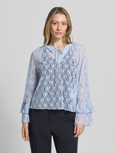Frauenmodel trägt Regular Fit Langarmbluse in Spitzen-Optik Modell 'LOULOU' von Vero Moda in zartem Hellblau, semitransparente Optik, V-Ausschnitt, Schleifenband, Trompetenärmel, Materialverarbeitung Spitze, Ganzkörperansicht von vorne.