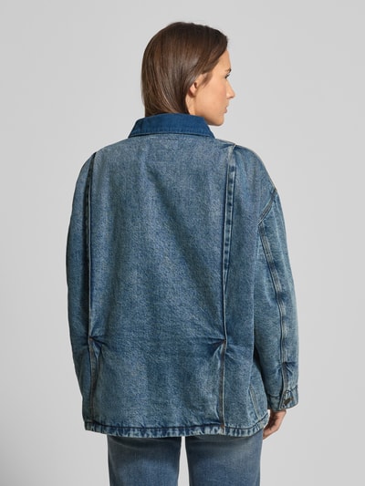 Kobiece model prezentuje kurtkę jeansową z bawełny, krój relaxed fit, model 'JOYBIRD' od American Vintage, długość tyłu 61 cm, szerokość ramion 56 cm, szerokość klatki piersiowej 68 cm, długość rękawów 55 cm, wykładany kołnierz, listwa guzikowa, kieszenie na piersi i wpuszczane kieszenie, widok całej sylwetki od tyłu.
