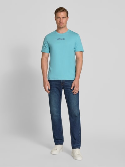 Mężczyzna nosi Regular Fit T-Shirt aus reiner Baumwolle od s.Oliver RED LABEL, jednolity kolor, krój regular fit, napis, okrągły dekolt, krótki rękaw, jersey, bawełna, całopostaciowy widok z przodu.