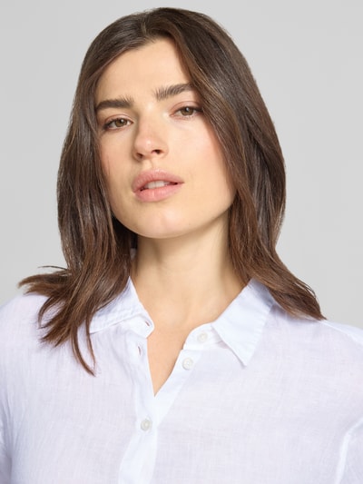 Frauenmodel trägt Hemdbluse aus Leinen mit Kentkragen Modell 'MIRA' von 0039 Italy, weiß, glatte Struktur, Nahaufnahme Oberkörper. Reines Leinen, Regular Fit, Knopfleiste, Sportmanschetten, Rückenlänge bei Größe S 68 cm, Ärmellänge 62 cm.
