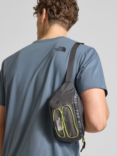 Männermodel trägt Bauchtasche mit Label-Stitching Modell 'JESTER LUMBAR' von The North Face, schwarz-grau mit gelben Details, Hauptfach mit Reißverschluss, Größenverstellbar, Ganzkörperansicht Rückansicht.