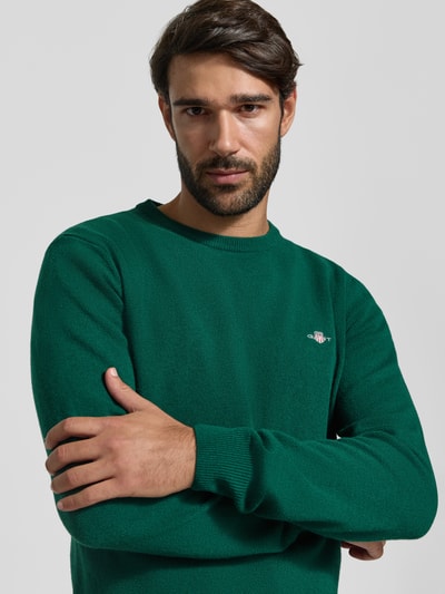 Mężczyznę model prezentuje zielony sweter o kroju regular fit z czystej wełny Regular Fit Pullover aus reiner Wolle od GANT, ujęcie z przodu w zbliżeniu na górną część ciała