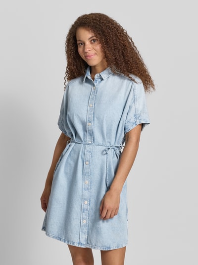 Frauenmodel trägt Relaxed Fit Jeanskleid aus reiner Baumwolle von Marc O'Polo Denim, tkanina stylizowana na denim, krój relaxed fit, długość mini, wysokie zapięcie, wiązany pasek, kołnierzyk koszulowy, listwa guzikowa, krótki rękaw, materiał: bawełna, jasnoniebieski kolor, gładka faktura, Ganzkörperansicht von vorne.