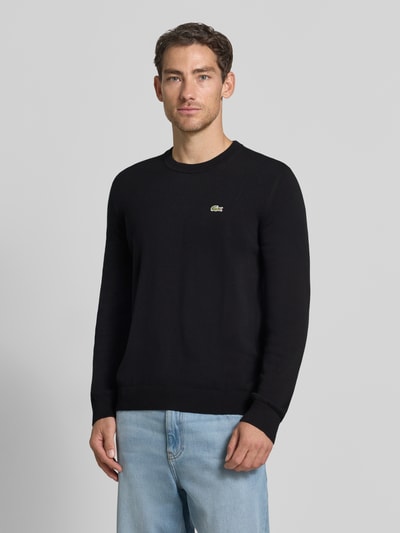 Männermodel trägt schwarzen Regular Fit Pullover aus Baumwoll-Mix von Lacoste, dezentes Logo, glatte Struktur, Ganzkörperansicht von vorne. Herren Pullover von Lacoste.