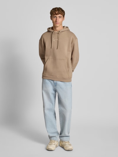 Męski model nosi Hoodie mit Label-Stitching od KARL KANI, bawełna, luźny krój, kaptur, kieszeń, jasne kolory, widok całej sylwetki z przodu.