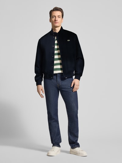 Männermodel trägt Regular Fit Bomberjacke mit Baumwoll-Anteil Modell 'HARRINGTON' von Lacoste, Optik: Unifarben, mit Stehkragen, verdecktem Reißverschluss, Knopfleiste, Logo-Stitching, geripptem Ärmel- und Rumpfabschluss, seitlichen Eingrifftaschen, Ganzkörperansicht von vorne.