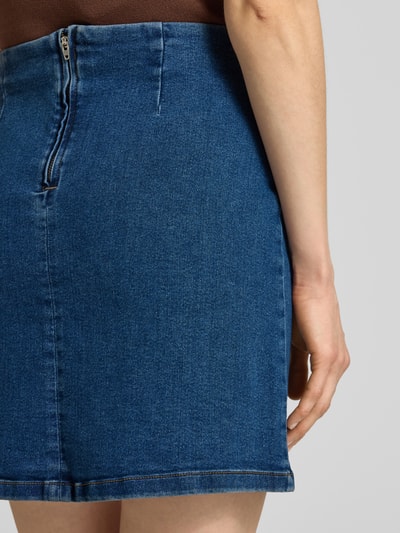 Frauenmodel trägt eng anliegenden Jeansrock aus Baumwoll-Mix Modell 'NELLY' von Vero Moda in Denim-Optik, Mini-Länge, Detailaufnahme Rückansicht.