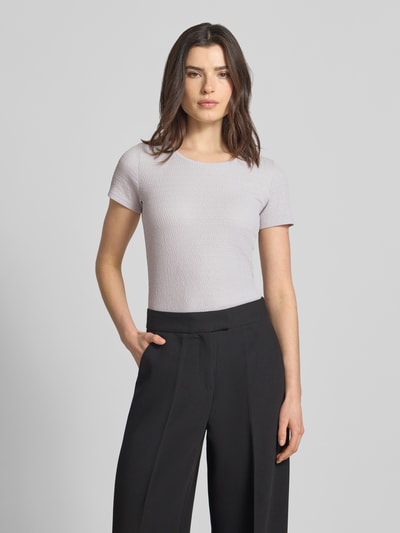 Vrouwenmodel draagt T-Shirt mit Label-Detail van Marc Cain in lichtgrijs, elastische materiaalmix, aansluitende fit, U-hals, detailopname bovenlichaam.
