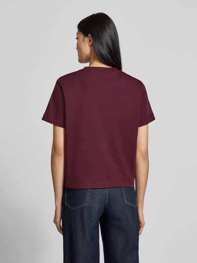 Männermodel trägt Damski t-shirt Boxy Fit T-Shirt aus reiner Baumwolle model 'SARA' von VERO MODA, bordowy kolor, prosta forma, gładka tekstura, Ganzkörperansicht Rückansicht.