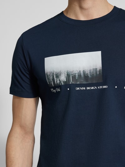 Männermodel trägt Regular Fit T-Shirt aus reiner Baumwolle von Tom Tailor Denim in Dunkelblau mit Foto- und Schriftzug-Print, Nahaufnahme Oberkörper.