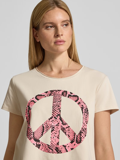 Frauenmodel trägt Relaxed Fit T-Shirt mit Motiv-Print Modell 'Peace' von miss goodlife, Beige mit pink-schwarzem Print, Nahaufnahme Oberkörper. Baumwoll-Mix, Rundhalsausschnitt, Rückenlänge 66 cm bei Größe S.