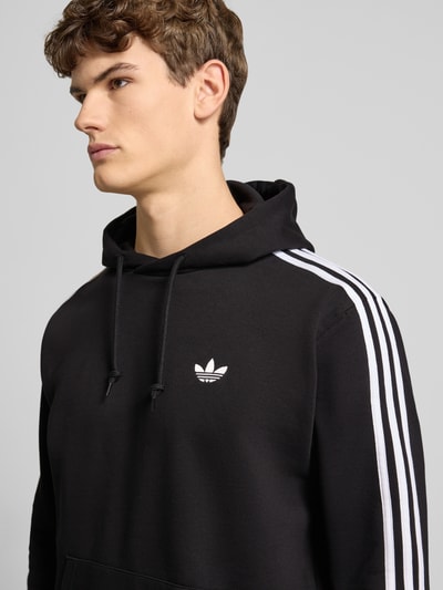 Männermodel trägt Hoodie mit Kapuze von adidas Originals in Schwarz mit weißen Streifen, Baumwoll-Mix, Nahaufnahme Oberkörper.