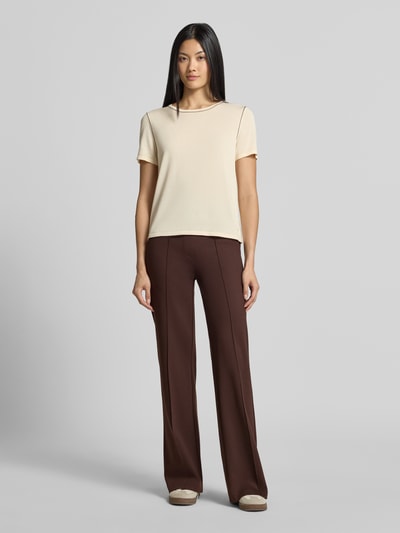 Frauenmodel trägt Straight Fit Stoffhose mit Viskose-Anteil von Smith and Soul in Dunkelbraun, sichtbar Bundfalten, Eingrifftaschen, elastischer Bund, kombiniert mit hellbeigem Shirt, glatte Struktur, Ganzkörperansicht von vorne.