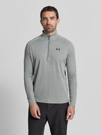 Männermodel trägt Funktionsshirt mit Logo und Reißverschluss von Under Armour in Grau, Regular Fit, Stehkragen, Ganzkörperansicht von vorne.