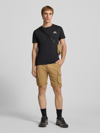 Männermodel trägt Shorts mit Cargotaschen Modell 'CREW SHORT' von Alpha Industries aus Baumwoll-Elasthan-Mix, Regular-Fit, sandfarben, Ganzkörperansicht von vorne. Kontext: Herren Shorts, Bundweite bei Größe 32 44 cm, Innenbeinlänge 22 cm.