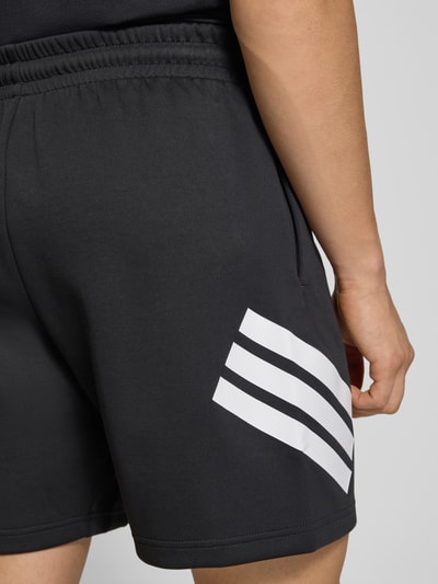 Mężczyzna nosi Regular Fit Sport-Shorts mit Logo-Print od adidas Sportswear, czarne, jednolity kolor, elastyczny pas, boczne kieszenie, nadruk logo, detaliczne ujęcie biodra