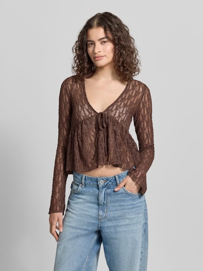Frauenmodel trägt Shaped Fit Blusentop mit Bindeverschluss Modell 'LAYA' von Only, Semitransparent, Mesh-Optik, abstraktes Muster, Langarm, ohne Kragen, tiefer V-Ausschnitt, Taillengürtel zum Binden, Materialverarbeitung: Mesh, Farbton Braun, Ganzkörperansicht von vorne.