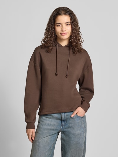 Frauenmodel trägt Regular Fit Hoodie aus Baumwoll-Mix Modell 'CHILLI' von PIECES in Dunkelbraun, glatte Struktur, Ganzkörperansicht von vorne.