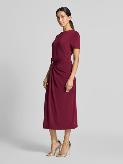 Frauenmodel trägt Midikleid mit Zierschnalle Modell 'Justine' von VILA in dunklem Rot, tailliert, elastisch, kurzärmelig, Ganzkörperansicht von vorne.