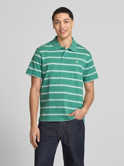 Männermodel trägt Regular Fit Poloshirt mit Logo-Stitching von Calvin Klein Jeans, grün mit weißen Streifen, Reine Baumwolle, Ganzkörperansicht von vorne.