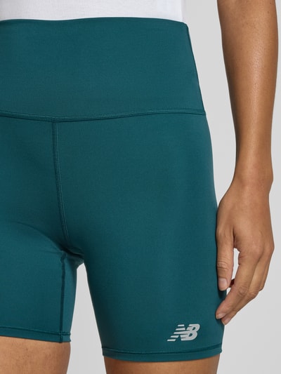 Frauenmodel trägt High Rise Radlerhose Modell 'HARMONY' von New Balance in Petrol mit elastischem Bund, Material-Mix mit Stretch, Nahaufnahme Oberschenkel.