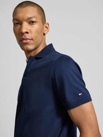 Männermodel trägt Regular Fit Poloshirt aus reiner Baumwolle von Tommy Hilfiger, unifarben in Dunkelblau, Logo-Detail, Nahaufnahme Oberkörper.
