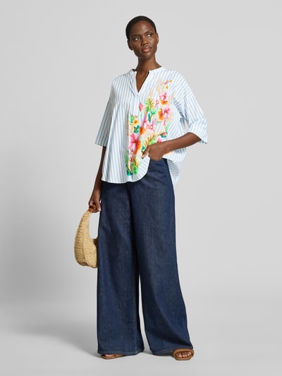 Kobiece model nosi Relaxed Fit Bluse mit Motiv-Print od Emily Van den Bergh, bawełna, krój relaxed fit, nadruk z motywem, dekolt w serek, rękaw o dł. 1/2, długość tyłu w rozmiarze 36: 48 cm, długość rękawów w rozmiarze 36: 24 cm, widok całej sylwetki z przodu.