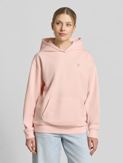 Vrouwenmodel draagt Oversized Hoodie met strass-steentjes model 'Silvy' van Guess Activewear in zachtroze, katoenmix, oversized fit, met capuchon, kangoeroezak en elastische boorden. Ganzkörperaanzicht van voren.