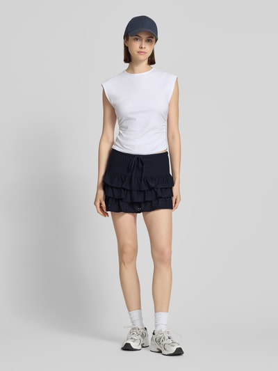 Frauenmodel trägt Leicht ausgestellter Mini-Skort mit Lochstickerei Modell 'SMILLA' von Only in dunklem Unifarben, strukturierte Optik, Rüschen und elastischer Bund mit Tunnelzug, Mini-Länge, Volant-Saum, Ganzkörperansicht von vorne.