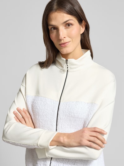 Frauenmodel trägt Regular Fit Sweatjacke mit Strickbesatz von Marc Cain in Offwhite, Stehkragen, Zweiwege-Reißverschluss, Nahaufnahme Oberkörper.